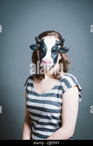 Jeune femme portant un masque sur fond gris en studio Banque D'Images