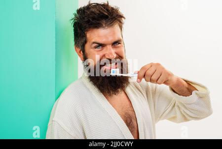 Homme se brossant les dents avec une brosse à dents et de la pâte à tootpate. Soins buccaux. Hygiène dentaire. Homme barbu en peignoir. Banque D'Images