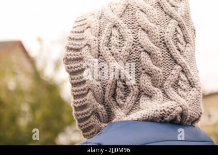 Effet de flou artistique sur la capuche en maille à l'extérieur, vue arrière. Gros plan. Une jeune femme dans un capot se tient avec son dos à la caméra sur un fond. Hors foyer. Banque D'Images