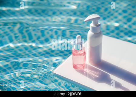 Bouteille de sérum, crème solaire, crème solaire sur fond de piscine d'eau le jour d'été cosmétiques avec pour hydrater Banque D'Images