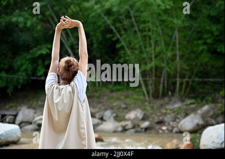 Une femme asiatique détendue et paisible s'étirant les bras, profitant de la belle vue sur la nature et prenant un souffle profond pour l'air frais de la nature du matin. Banque D'Images