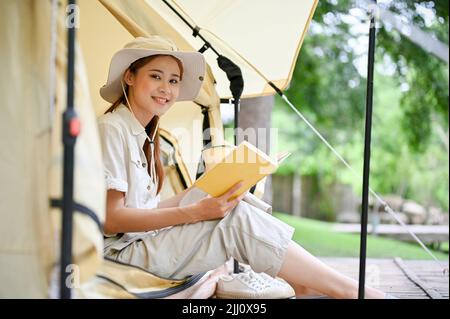 Belle et charmante jeune femme asiatique campeur assis dans sa tente avec son livre préféré dans le terrain de camping. Concept Camping Banque D'Images