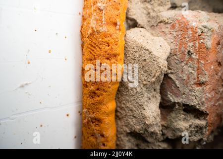 Vieille mousse de polyuréthane orange entre le mur et la fenêtre en plastique gros plan Banque D'Images