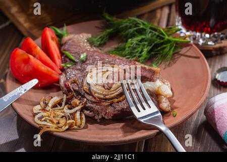 Délicieux dîner copieux préparé par un homme. Concentrez-vous sur un morceau de steak de bœuf marbré à la fourchette. Viande, bière, tomates et aneth pour un repas complet. Banque D'Images