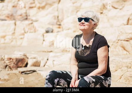 Vieille femme vêtue de noir assise sur un rocher près de la mer Banque D'Images