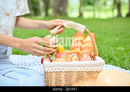 En gros plan, Une belle femme est assise sur une couverture de pique-nique et tient un panier en osier pour pâtisseries. Banque D'Images