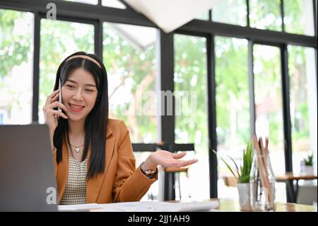 Une femme d'affaires asiatique ou une employée de marketing attirante et professionnelle parlant au téléphone avec son client tout en regardant les détails Banque D'Images