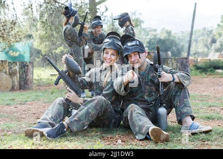 Joyeux joueurs de paintball hommes et femmes assis sur le sol avec des fusils à l'extérieur Banque D'Images