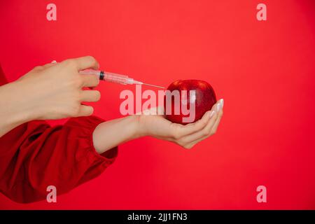 Femme rognée main avec seringue appliquer l'injection à la pomme rouge juteuse fraîche dans le studio rouge. Botox, injection hyaluronique ad Banque D'Images