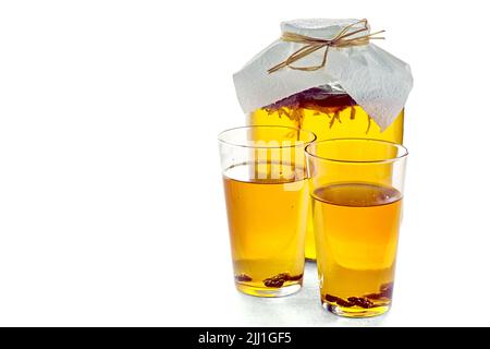 Jarre de kombucha et deux verres de kombucha avec des raisins secs isolés sur un fond blanc sur une table en béton gris clair. Boisson gazeuse à faible teneur en alcool o Banque D'Images