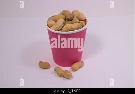 Décortiqueter les arachides dans une tasse en papier sur une surface blanche Banque D'Images