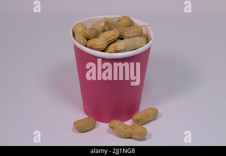 Décortiqueter les arachides dans une tasse en papier sur une surface blanche Banque D'Images