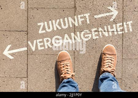 Chaussures marron avec texte indiquant les directions vers l'avenir ou le passé en allemand sur un terrain Banque D'Images