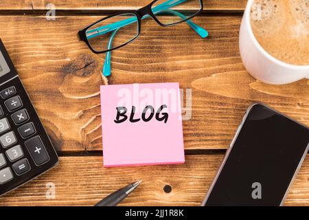 Bureau avec texte de blog sur papier rose entouré d'une calculatrice, d'un smartphone et de lunettes Banque D'Images
