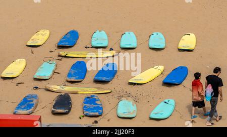 Rangées de planches de surf avec deux surfeurs marchant devant la plage de long Sands, Tynemouth, North Tyneside, Royaume-Uni Banque D'Images