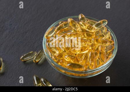Capsules d'huile de poisson de foie de morue dans un bol en verre sur fond de plaque d'ardoise noire. Omega 3, suppléments de vitamine E. Concept de régime alimentaire sain. Gros plan, espace de copie Banque D'Images