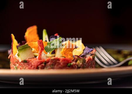 Une belle tartare de thon fraîchement préparée, avec des légumes doux/aigre, de la mayonnaise à la chaux, de la vinaigrette orientale et des chips de nori. Avec fourche. Banque D'Images