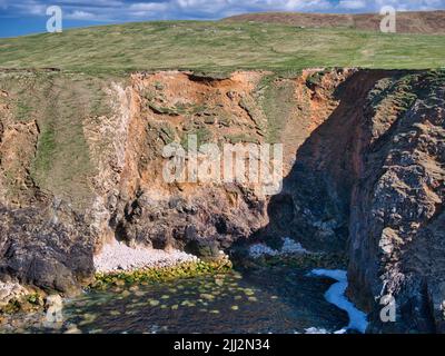 Perte des terres côtières causée par l'érosion des terres et le glissement dans la mer. Prise près d'Uyea dans Northmavine, Shetland, Royaume-Uni, par une journée ensoleillée avec un ciel bleu. Banque D'Images