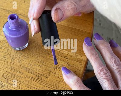 Grand-mère âgée qui polissage ses ongles avec un vernis violet Banque D'Images