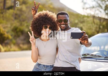 Elle ne l'a pas encore vu. Un jeune couple qui prend un selfie pendant un voyage en voiture. Banque D'Images