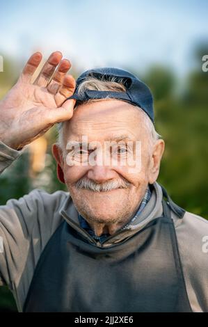 Portrait d'un homme de 88 ans dans une casquette de baseball avec sa main levée en saluant. Bonne vieillesse active. Banque D'Images