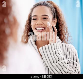 Donnez un peu d'amour à votre visage. Une jeune femme attrayante appliquant de la lotion sur son visage dans la salle de bains à la maison. Banque D'Images