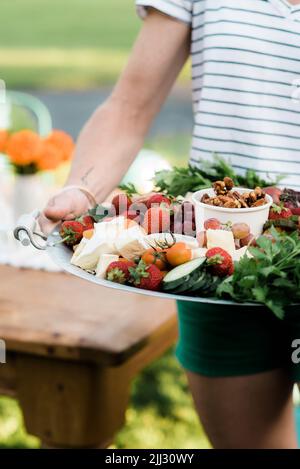 Gros plan vertical de la femme à l'extérieur en été, avec un plateau de nourriture vers le spectateur avec table en bois d'été pour dîner à l'extérieur. Banque D'Images