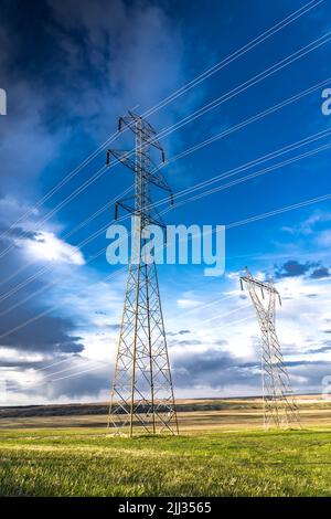 De grandes tours de transmission en acier de grande taille fournissent de l'électricité et de l'Internet rural aux résidents de l'Alberta le long des champs agricoles des Prairies dans les Rocheuses Banque D'Images