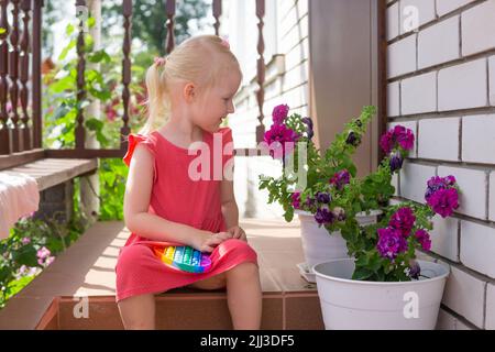 Mignon caucasien équitable cheveux fille dans la robe rose est de jouer et de montrer drôle tendance silicone antistress coloré jouet popit. Le jouet de violon Push Popper est le Banque D'Images