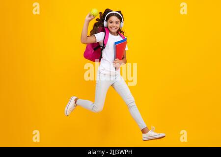 Enfant d'école, jeune fille étudiante avec casque et sac à dos d'école sur fond jaune isolé studio. Concept de l'école et de l'éducation des enfants. Banque D'Images