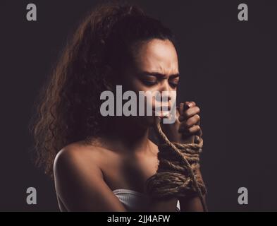 Je me détruis si les autres ne peuvent pas. Une jeune femme regardant peur avec une corde attachée autour de ses bras sur un fond noir. Banque D'Images