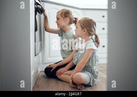 Les inspecteurs certifiés des cookies attendent patiemment leurs gâteries. Deux petites filles vérifient ce qui cuit dans un four à la maison. Banque D'Images