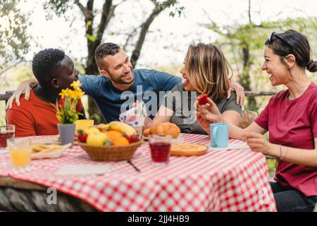 Un groupe d'amis gais et multiraciaux se réunissent au restaurant de la ferme et s'amusent à manger des fruits au brunch - les gens, en bonne santé et en plein air style de vie Banque D'Images