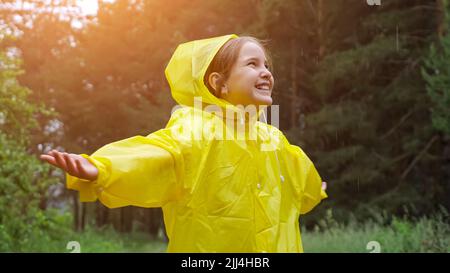 Une fille gaie en imperméable se répand les mains attrapant les gouttes de pluie Banque D'Images