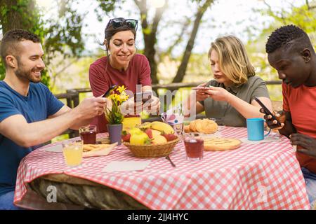 Groupe d'amis multiethniques ayant le plaisir de prendre des photos de nourriture assis à table de pique-nique - blogueur de nourriture et influenceurs wannabe concept Banque D'Images