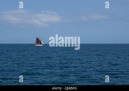 un voilier aux voiles brunes navigue sur une mer bleue calme par une belle journée ensoleillée Banque D'Images