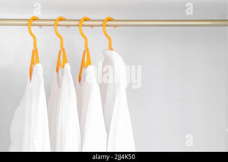 Chemises blanches accrochées sur le porte-vêtements de l'armoire. Vêtements féminins différents sur des porte-affiche jaunes Banque D'Images