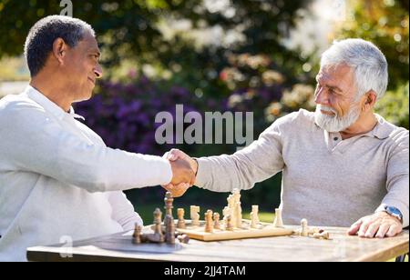 Bien joué. Deux hommes assis à l'extérieur ensemble et serrer les mains après avoir joué à une partie d'échecs. Banque D'Images