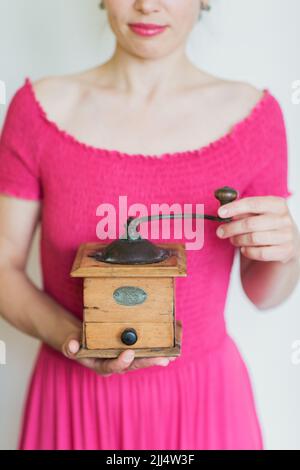 Belle femme souriante en robe rose tient un moulin à café manuel dans ses mains Banque D'Images