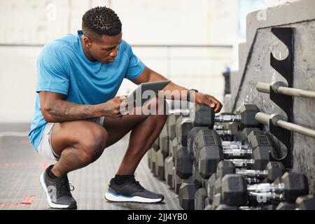 Tout doit être organisé dans ce gymnase. Un jeune homme musclé utilisant une tablette numérique tout en vérifiant l'équipement dans un gymnase. Banque D'Images
