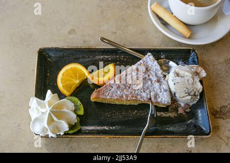 Gâteau aux amandes avec glace et fruits sur une assiette noire sur une table en marbre beige, délicieux dessert, vue de dessus, espace copie, sélection Banque D'Images