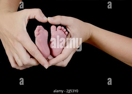 Les pieds du nouveau-né sont dans les mains en forme de cœur de sa mère. Concentrez-vous sur le pied et les mains sur la droite. Banque D'Images