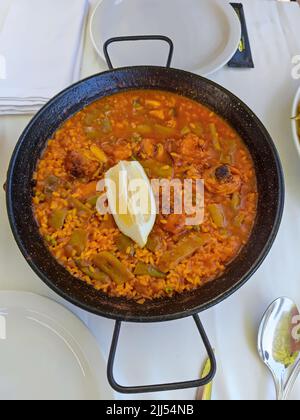 Une délicieuse paella avec des légumes, de la viande et un citron servi dans un restaurant Banque D'Images