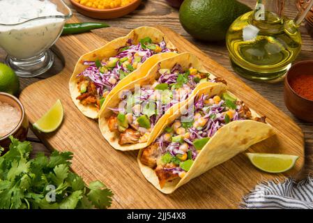 Tacos de poisson avec avocat, chou pourpre, maïs et lime sur une table en bois rustique ancienne. Banque D'Images