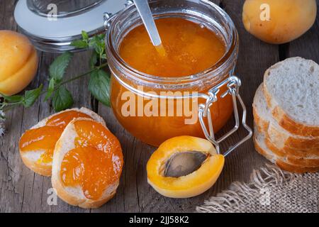 Confiture d'abricots dans un pot en verre et pain sur une vieille table en bois Banque D'Images