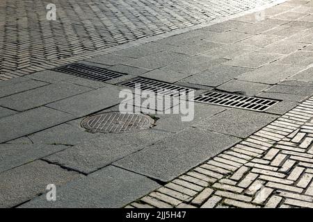 trou d'homme rond en fer avec trappes grilles rectangulaires du système de drainage sur la route avec bloc de pierre pavée près du trottoir piétonnier en br Banque D'Images