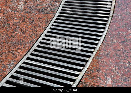 système de drainage incurvé avec bandes grille sur le sol en granit avec une surface en granit rouge humide en pierre, gros plan d'un système de tempête humide après la pluie Banque D'Images