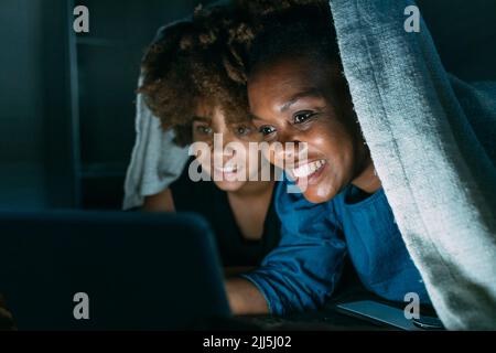 Bonne mère partageant un Tablet PC avec sa fille sous une couverture à la maison Banque D'Images