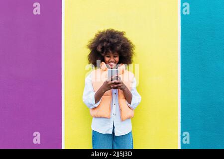 Bonne fille utilisant un smartphone debout devant un mur coloré Banque D'Images