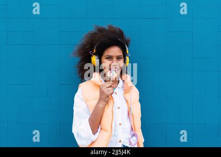 Une jeune fille qui se régale de la musique à l'aide d'un casque sans fil devant un mur bleu Banque D'Images